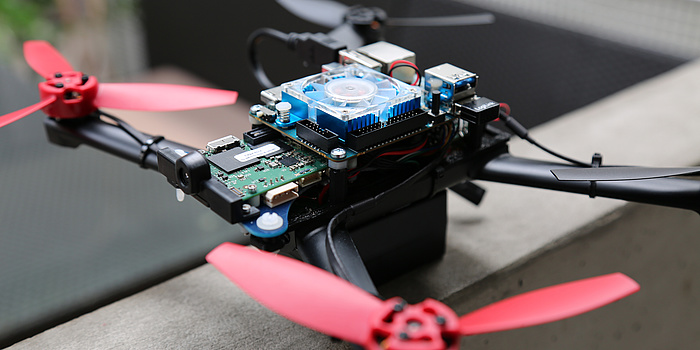 Ein schwarzes Drohnengestell, mit roten Propellern, einem blauen Ventilator und einer grünen Platte mit Schaltungen.