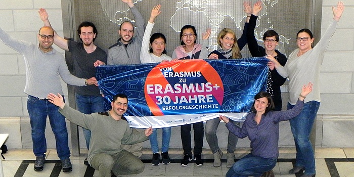 Staff and international students of TU Graz hold a colourful banner with the inscription “From Erasmus to Erasmus+ – a story of 30 years.”