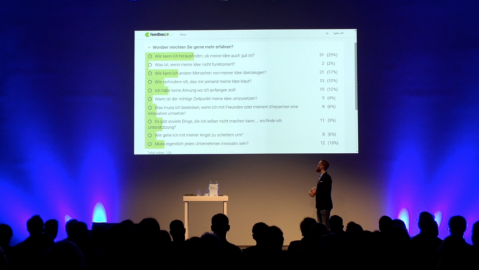 ein Vortragender präsentiert die feedbackr-App vor Publikum.