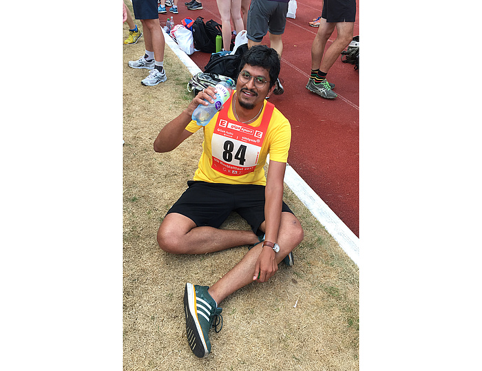 Exhausted but happy runner wearing a yellow shirt showing the start number 84 drinks from a bottle of water.