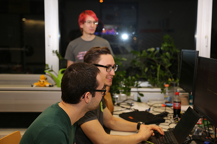 © Wiedner – TU Graz Two LosFuzzy guys working together on a computer in the nocturnal FuzzyLab, a third LosFuzzys member is to be seen in the background, watching.