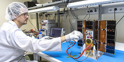 A man in a white coat is working on a satellite in a laboratory.