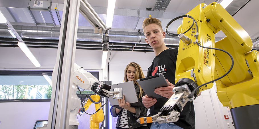 Zwei Studierende arbeiten mit einem Roboterarm.