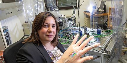 A woman looks into the camera. In front of her is a hand made of plastic with attached sensors