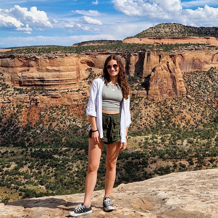 Eine Dame im Wanderoutfit steht vor einer roten Felsformation.