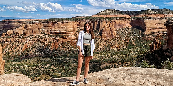A lady in a hiking outfit stands in front of a red rock formation.