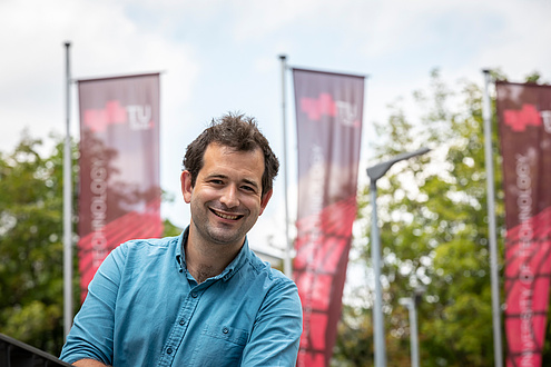 Portrait of a TU Graz researcher, TU Graz flags in the background