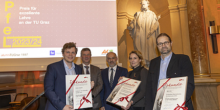 Five people smile into the camera, three of them hold a certificate showing them as winners.