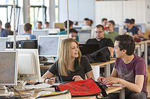 Young woman and young man chat in a room full of PCs.