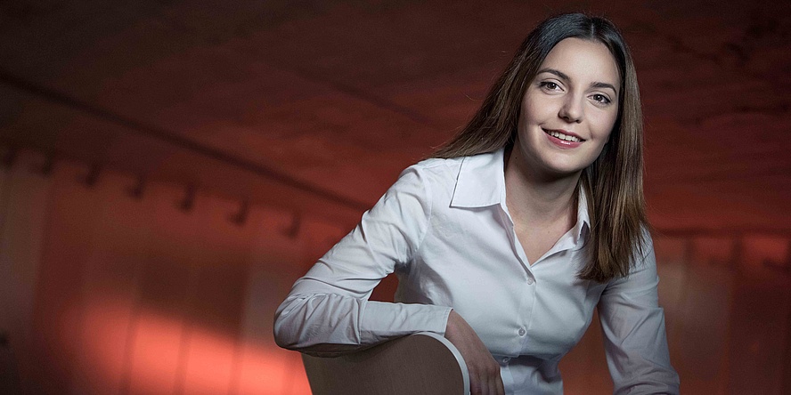 Young woman wearing a white blouse in front of a reddish lit wall.