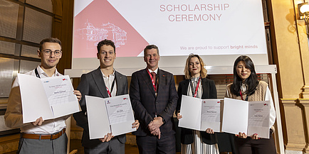 Five people stand next to each other and look into the camera, four of them holding certificates in their hands.