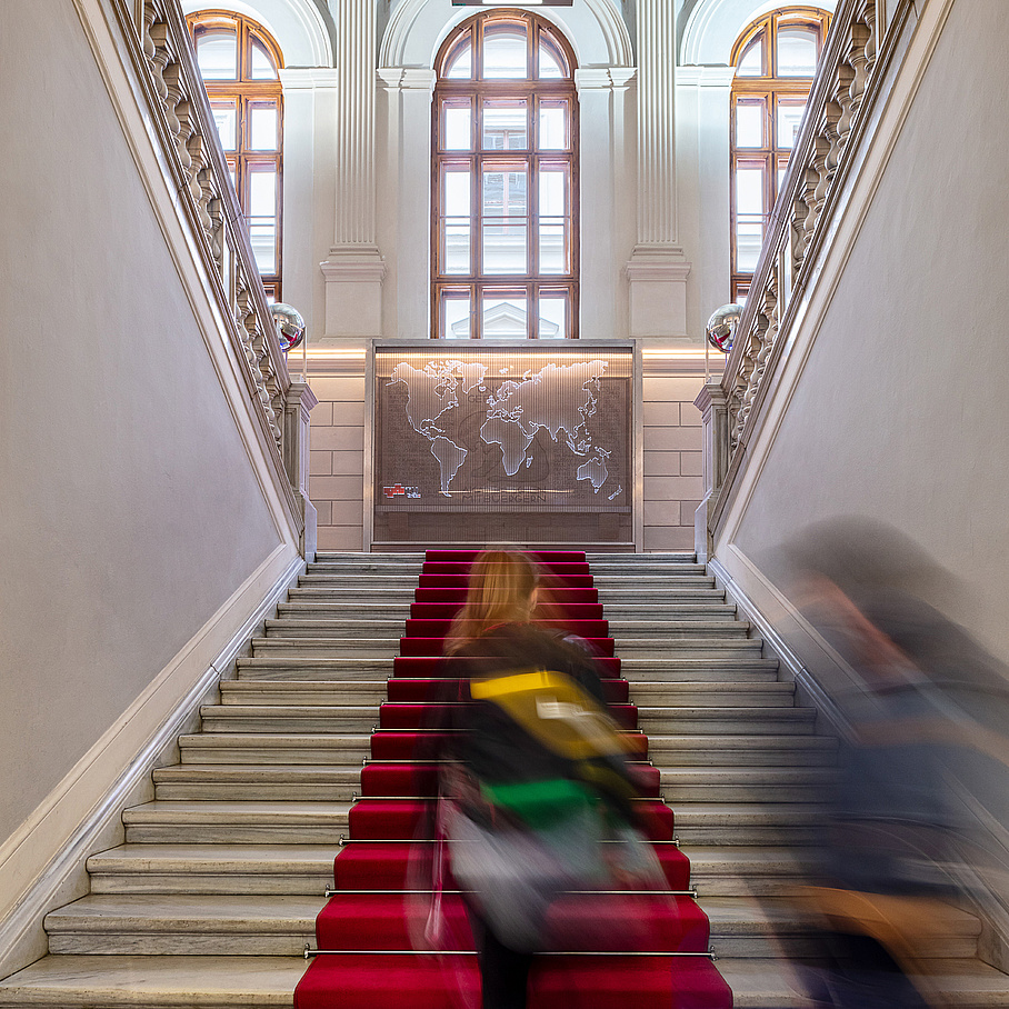 Personen gehen eine Treppe mit rotem Teppich hinauf