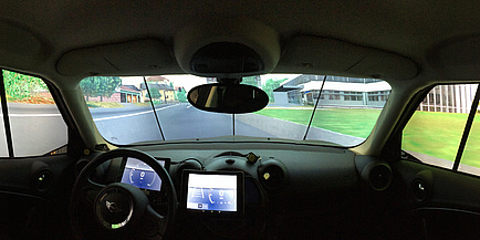 A view from the car cockpit, in the middle there is a tablet PC that functions as an instrument panel. The landscape behind the side windows and the windshield is virtual.  