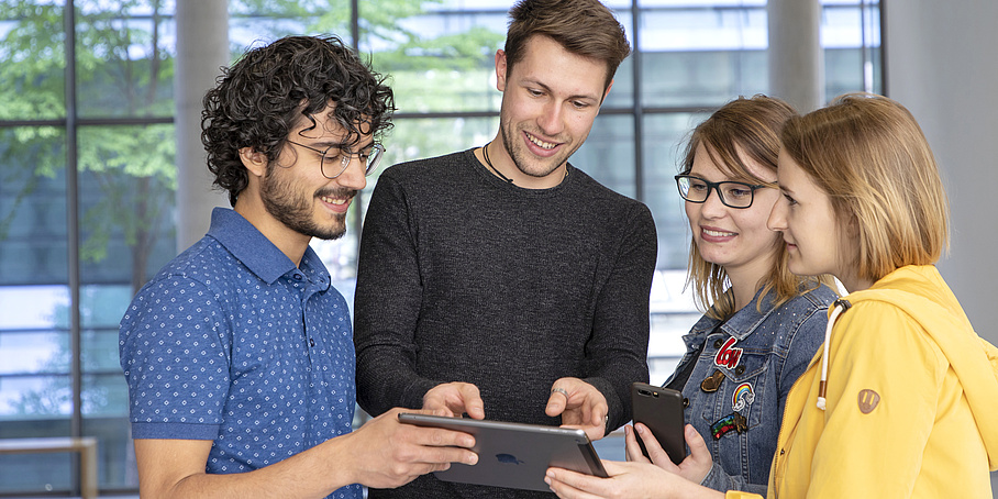 Vier Studierende schauen auf ein Tablet.