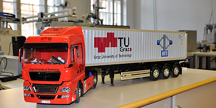 Ein Modell-Lkw mit rotem Führerhaus und weißem Container mit TU Graz Logo steht im Testlabor auf einem Tisch