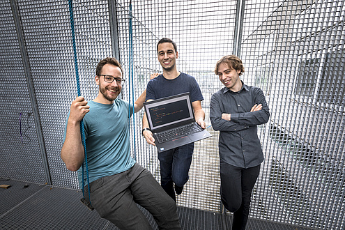 Drei Männer stehen auf einer Veranda, die mit Gitterwänden gesichert ist; Der linke Mann sitzt in einer Schaukel, der mittlere Mann hält einen Laptop in Händen r Schaukel, in der Mitte 