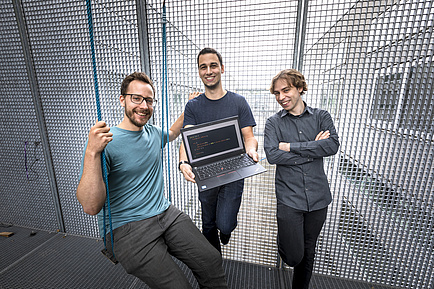 Three men stand on a veranda secured with lattice walls; the left man sits in a swing, the middle man holds a laptop in his hands r Swing, in the middle 