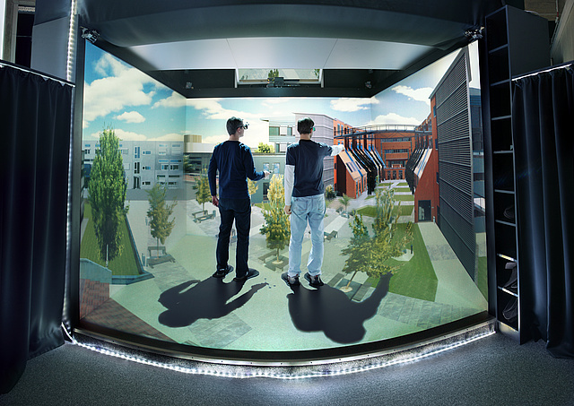 Das Bild zeigt 2 Personen, die in einem System zur Darstellung von dreidimensionalen virtuellen Inhalten stehen.