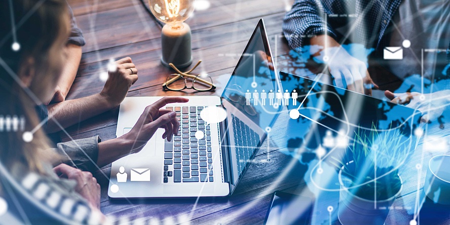 Close-up of the hands of three people at a table with a laptop. Symbols for the digital networking of people are graphically superimposed on the image.