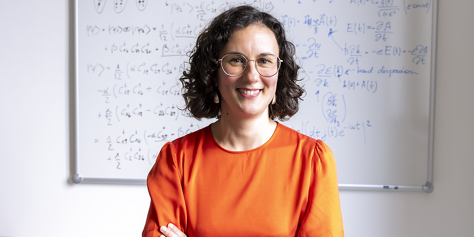 A portrait of Anna Galler in front of a whiteboard covered in equations.