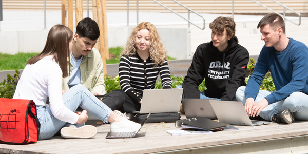 Junge Menschen sitzen auf Holzplattform mit Laptops