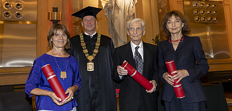 Vier Menschen, zwei Frauen und zwei Männer, lächeln in die Kamera. Sie sind feierlich gekleidet.