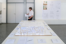 A man looks at paper city models on a large table.