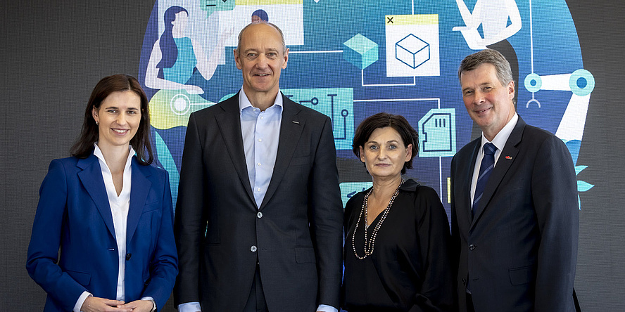 Four people stand in front of a colorful wall and smile at the camera.