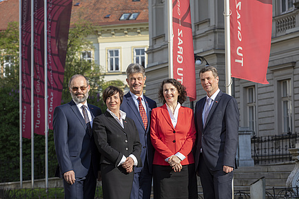 Das Rektoratsteam - zwei Frauen und drei Männer stehen vor der Technischen Universität, im Hintergrund sind die TU Graz-Fahnen zu sehen