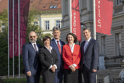 Das Rektoratsteam - zwei Frauen und drei Männer stehen vor der Technischen Universität, im Hintergrund sind die TU Graz-Fahnen zu sehen