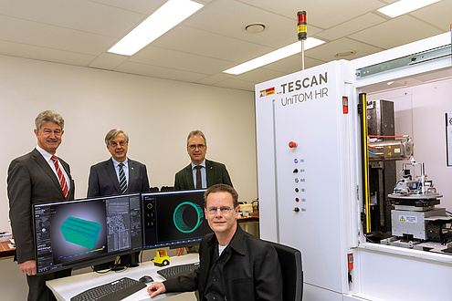 Four gentlemen next to two computer screens and a micro-CT chamber