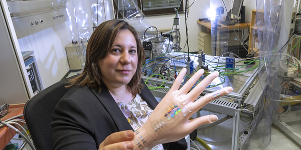 Lächelnde Frau hält eine künstliche menschliche Hand mit aufgeklebten Elementen.