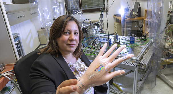 Smiling woman holding an artificial human hand with elements attached.