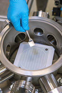 Hand in blue rubber glove puts by tweezers a small metal object into a big device.