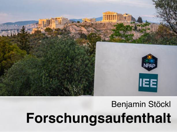 Laptop mit NPAP- und IEE-Aufklebern vor der Akropolis in Athen, umgeben von grünen Bäumen und beleuchtetem Parthenon im Abendlicht, mit dem Text „Benjamin Stöckl Forschungsaufenthalt“.