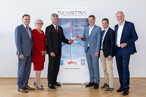 Six people are standing in front of a banner and are looking into the camera.