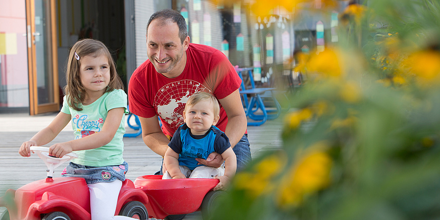 A TU Graz employee with daughter and son on the on the outdoor area of the TU Graz nanoversity, part of the public childcare facility at Campus Inffeldgasse.