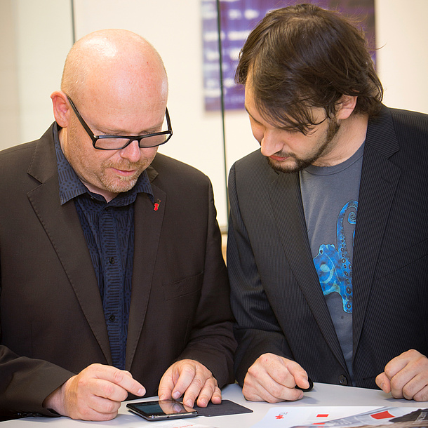 Two men regarding the screen of a mobile phone. Photo source: Lunghammer - TU Graz