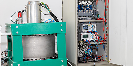 A cylindric cask which contains a fly wheel energy storage device stands next to a computer rack