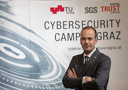 A man in a suit stands in front of the expo wall of the Cybersecurity Campus Graz