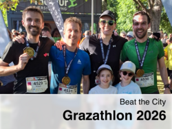 Four happy runners with medals and two children pose after the Grazathlon 2026 “Beat the City” in front of a crowd in a green outdoor setting.