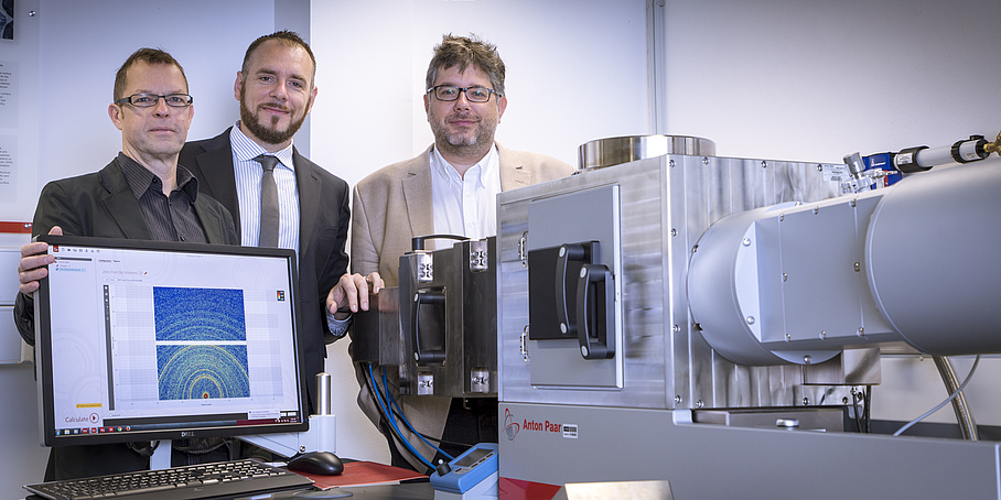 Three researchers grouped around a laboratory instrument