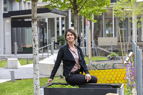 A woman sits on a bench outside and smiles at the camera.