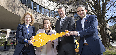 Vier Personen lächeln in die Kamera, links zwei Frauen, rechts zwei Männer. Sie halten einen gelben Schlüssel gemeinsam in ihren Händen.