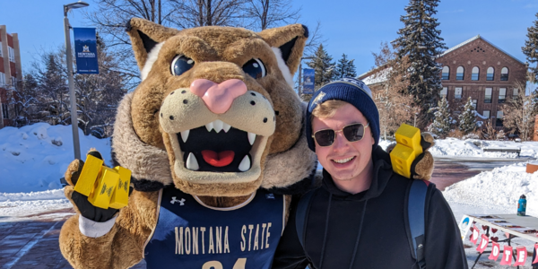 A man stands next to the bobcat Montana State University mascot.