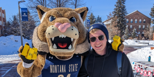 Ein Mann steht neben dem Rotluchs Montana State University Maskottchen.