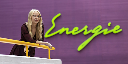 A woman leans against a railing. Behind her is written "Energy".