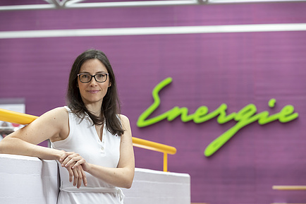A woman smiles into the camera. With her elbow she leans on a wall. Behind her the word Energy can be seen.
