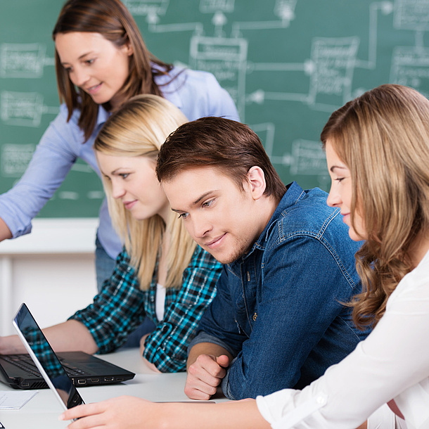 Young people in a classroom in front of a notebook.