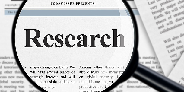 Eine Lupe vergrößert auf einer Zeitung das Wort "Research".